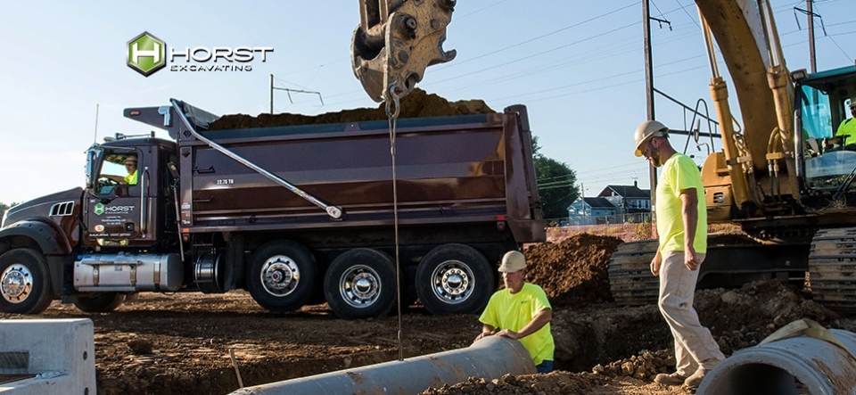 construction crew installing pipes on jobsite with excavating equipment