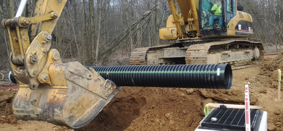 Track hoe digging soil around an underground utility pipe