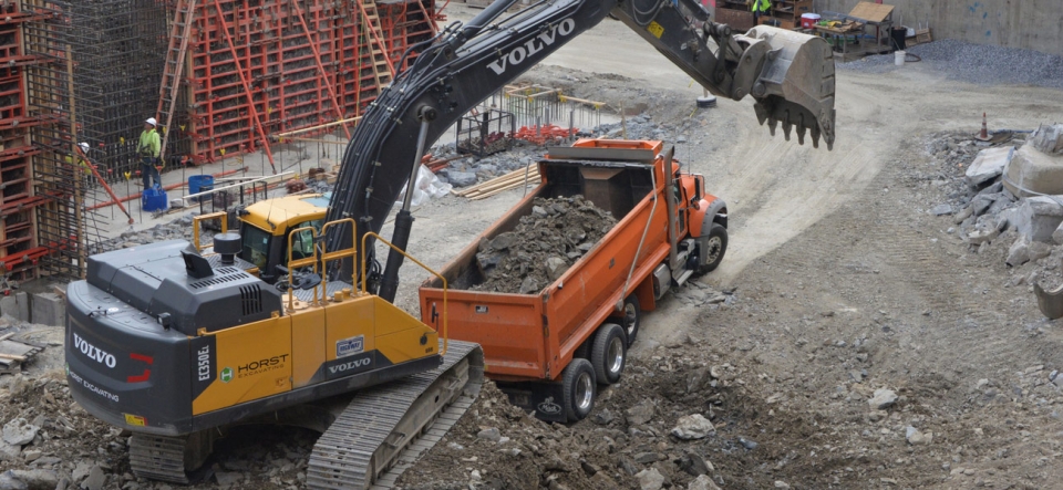 Track hoe loading dump truck on industrial excavation site