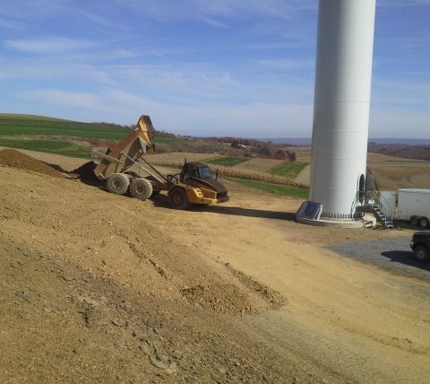 articulated dump truck dumping at base of wind turbine