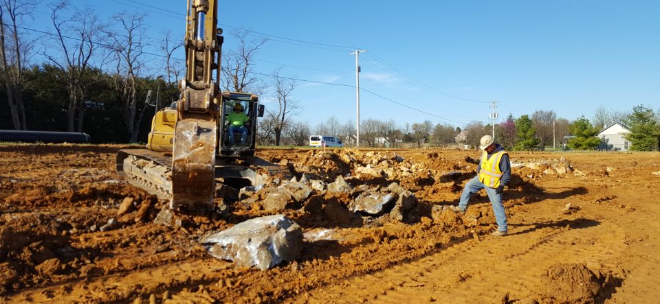 excavator removing large rocks on jobsite with person standing there