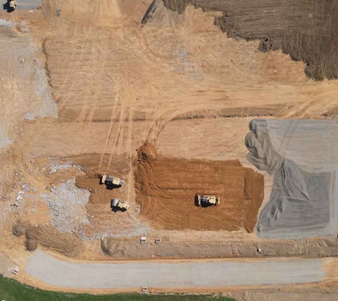 aerial view of bull dozers and rollers at in-progress construction site working on roadway