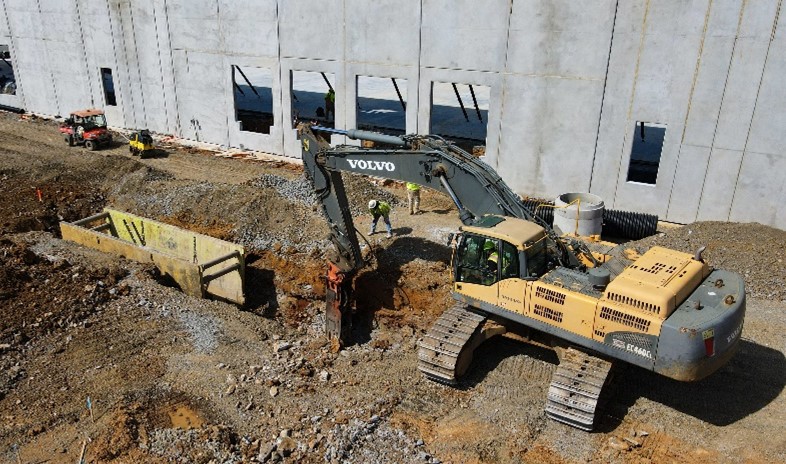 excavator digging trench with workers around